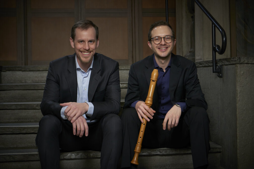 Benjamin Åberg och Per Gross sitter på ett trappsteg. De ler stort. Per har en blockflöjt i handen.