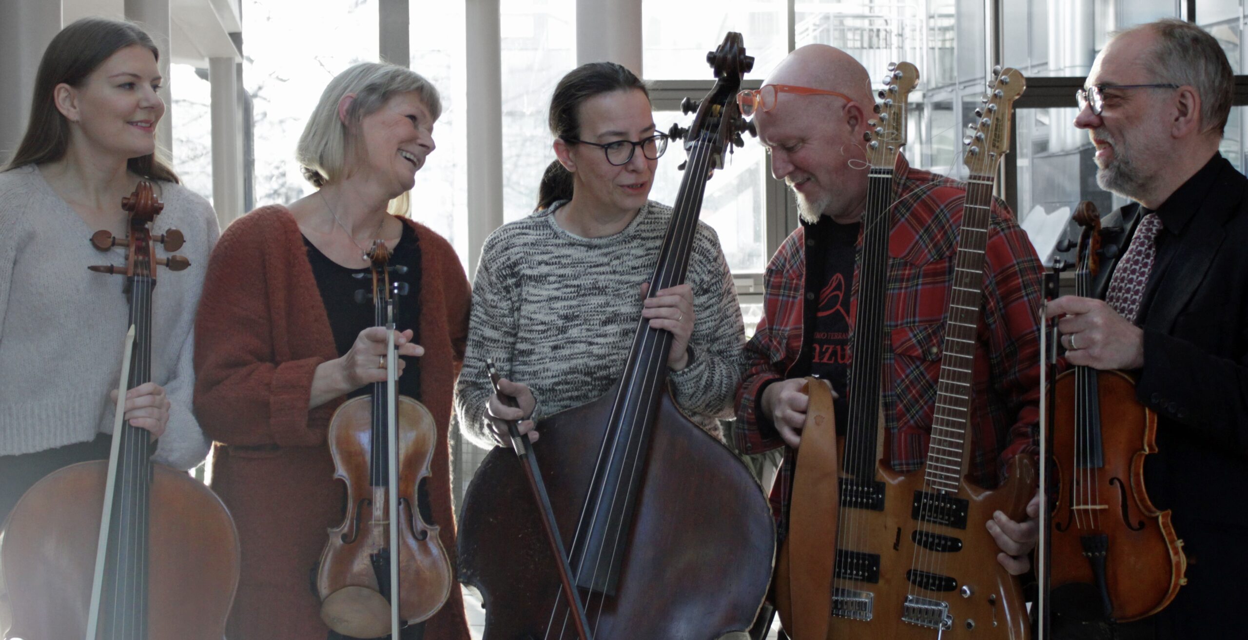 Kvintett Konstig på rad med sina instrument. Tina i mitten säger något roligt, övriga ler.